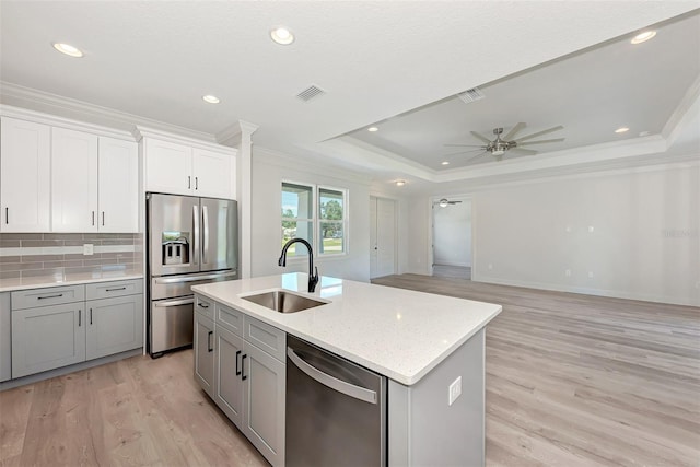 kitchen with sink, crown molding, a center island with sink, a raised ceiling, and stainless steel appliances