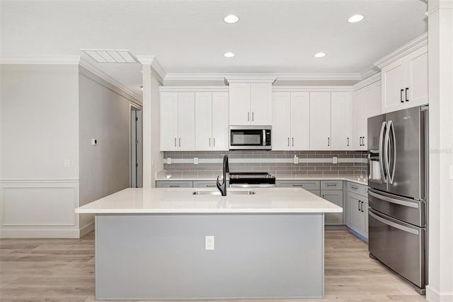 kitchen with stainless steel appliances, sink, a kitchen island with sink, and white cabinets