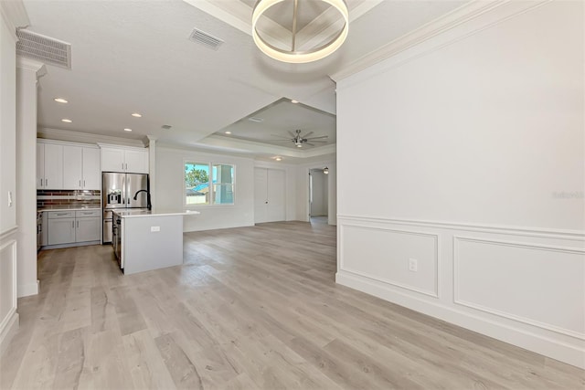 kitchen with ceiling fan, white cabinetry, ornamental molding, a center island with sink, and a raised ceiling