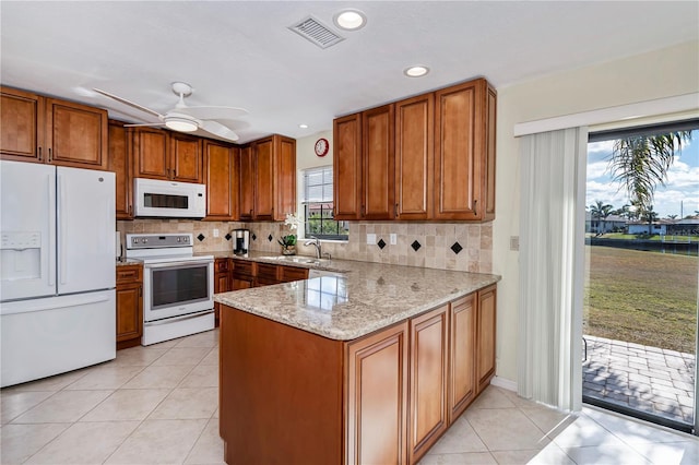 kitchen featuring sink, light tile patterned floors, light stone counters, kitchen peninsula, and white appliances