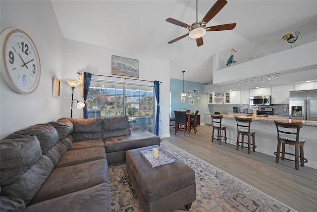 living room with vaulted ceiling, light hardwood / wood-style floors, rail lighting, and ceiling fan