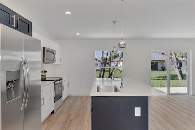 kitchen with sink, white cabinetry, decorative light fixtures, appliances with stainless steel finishes, and a kitchen island with sink