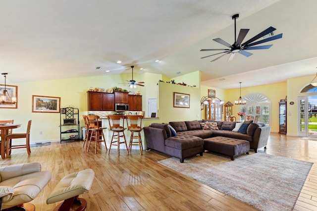 living room with ceiling fan with notable chandelier, lofted ceiling, and light hardwood / wood-style floors