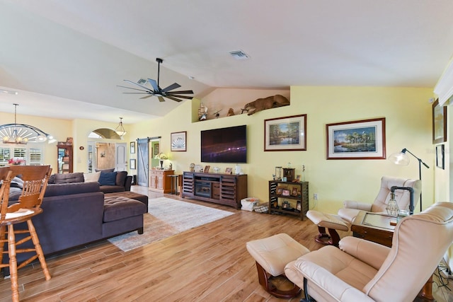 living room with ceiling fan with notable chandelier, vaulted ceiling, light hardwood / wood-style floors, and a barn door