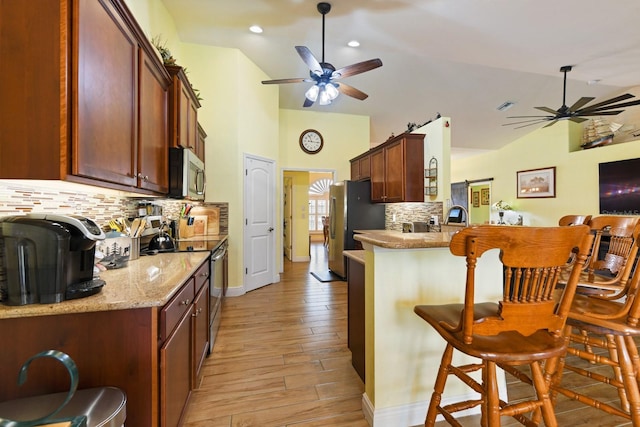 kitchen with vaulted ceiling, appliances with stainless steel finishes, tasteful backsplash, a breakfast bar area, and light wood-type flooring