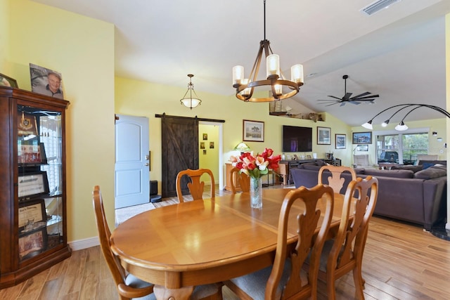 dining room featuring a barn door, ceiling fan with notable chandelier, lofted ceiling, and light hardwood / wood-style floors