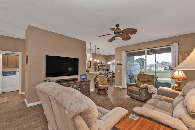 living room with hardwood / wood-style flooring, washer and dryer, and ceiling fan with notable chandelier