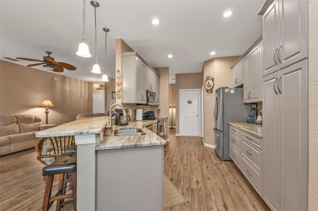 kitchen with sink, light wood-type flooring, appliances with stainless steel finishes, kitchen peninsula, and pendant lighting