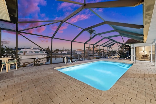 pool at dusk with a dock, a patio, a water view, and glass enclosure