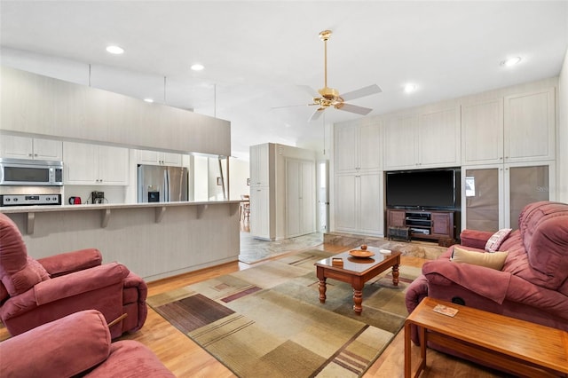 living room featuring ceiling fan, a towering ceiling, and light hardwood / wood-style floors