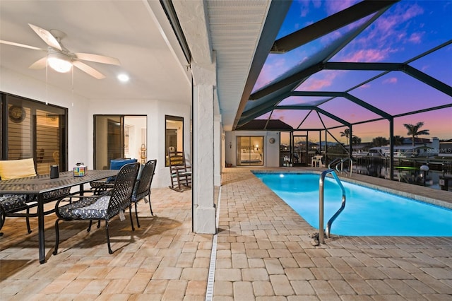 pool at dusk featuring a patio, ceiling fan, and glass enclosure