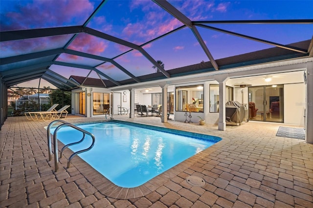 pool at dusk featuring a lanai, a patio area, and ceiling fan