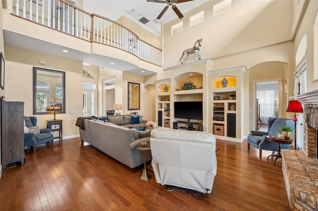 living room with ceiling fan, a brick fireplace, built in features, and dark hardwood / wood-style flooring