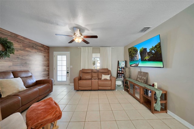 tiled living room featuring ceiling fan, wooden walls, and a textured ceiling