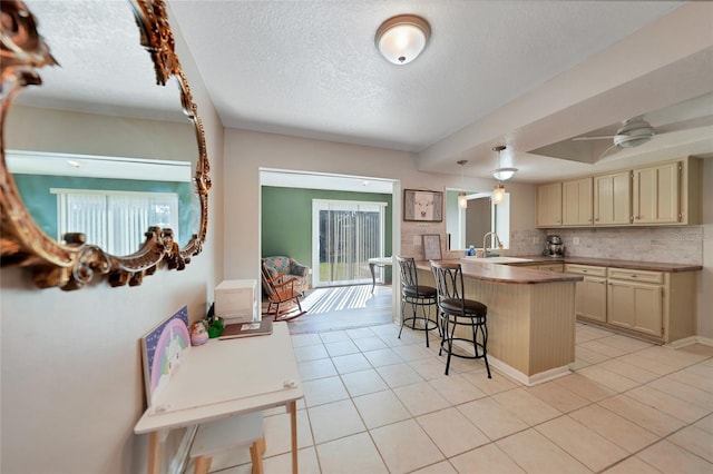 kitchen featuring sink, light tile patterned floors, a kitchen breakfast bar, tasteful backsplash, and cream cabinetry