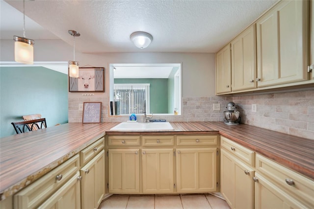 kitchen featuring sink, light tile patterned floors, butcher block countertops, and decorative light fixtures