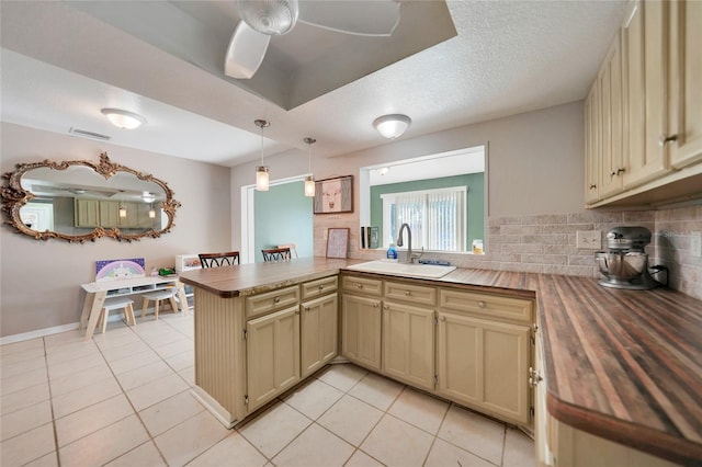 kitchen featuring sink, decorative backsplash, light tile patterned floors, kitchen peninsula, and cream cabinets