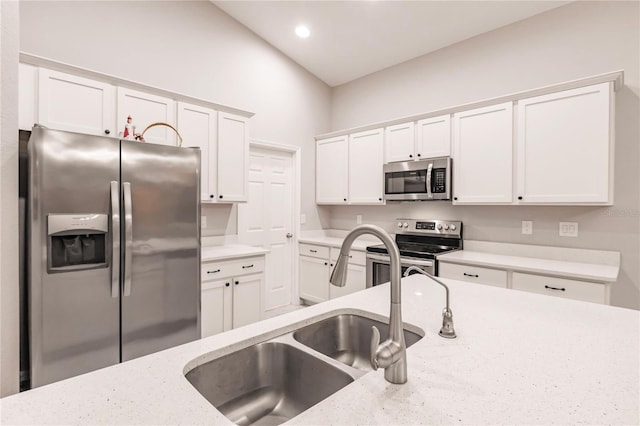 kitchen featuring lofted ceiling, sink, appliances with stainless steel finishes, light stone countertops, and white cabinets