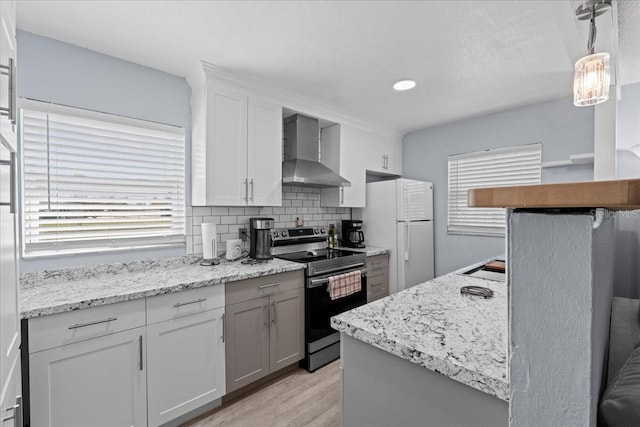 kitchen featuring decorative light fixtures, tasteful backsplash, stainless steel range with electric cooktop, white refrigerator, and wall chimney exhaust hood