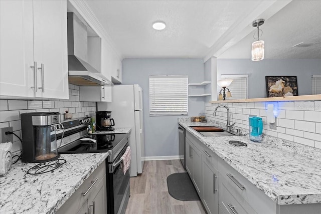 kitchen featuring wall chimney exhaust hood, sink, appliances with stainless steel finishes, pendant lighting, and light hardwood / wood-style floors