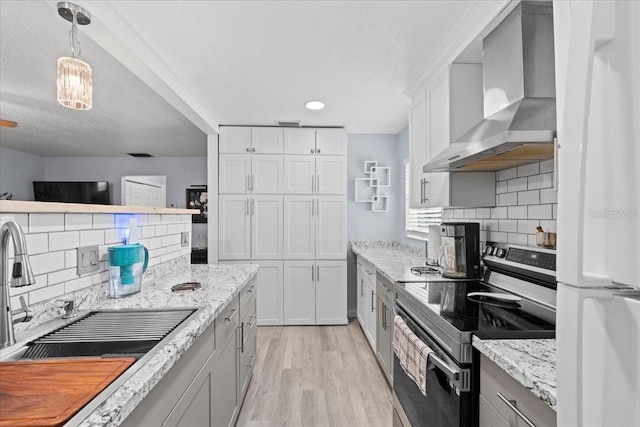 kitchen with wall chimney exhaust hood, sink, stainless steel range with electric cooktop, hanging light fixtures, and white cabinets