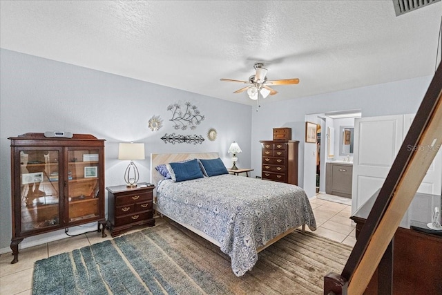 bedroom with ensuite bathroom, light tile patterned floors, ceiling fan, and a textured ceiling