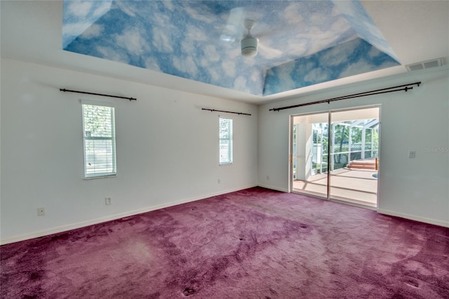 carpeted spare room with ceiling fan, plenty of natural light, and a tray ceiling