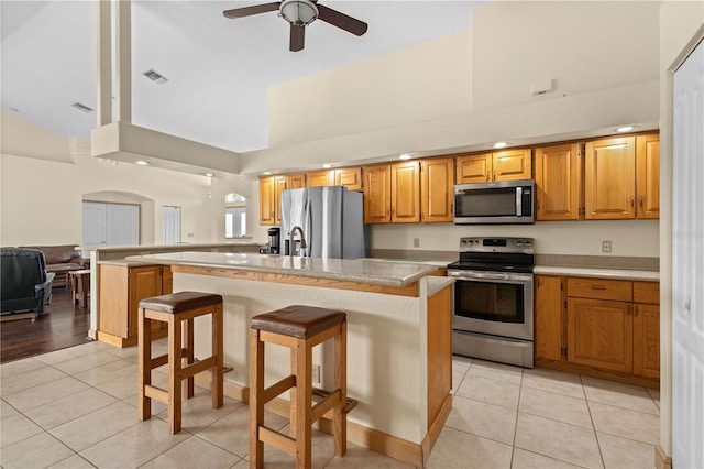 kitchen with ceiling fan, a kitchen breakfast bar, stainless steel appliances, a center island, and light tile patterned flooring