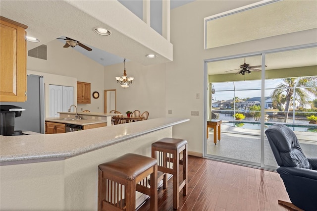 kitchen featuring vaulted ceiling, ceiling fan with notable chandelier, stainless steel dishwasher, kitchen peninsula, and a water view