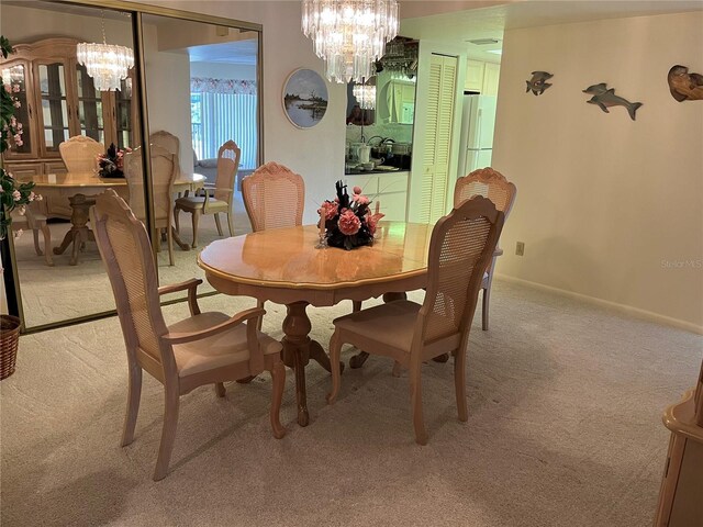 dining room featuring a chandelier, light colored carpet, and baseboards