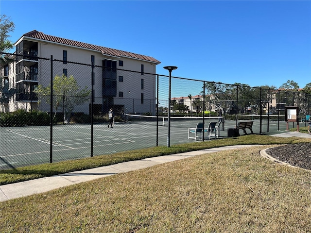 view of tennis court with fence and a lawn