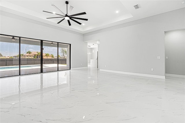 unfurnished room with ceiling fan, visible vents, baseboards, marble finish floor, and a tray ceiling