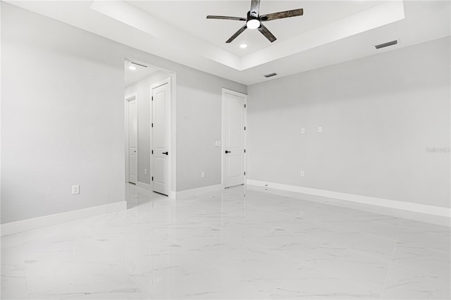 unfurnished room with a tray ceiling, marble finish floor, visible vents, a ceiling fan, and baseboards