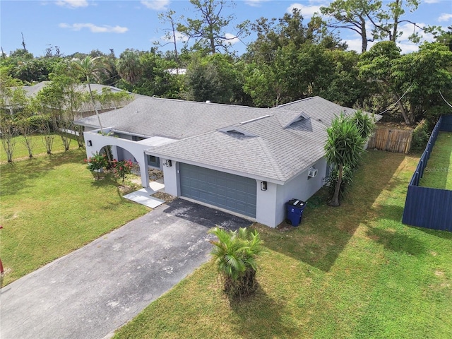 view of front of house featuring aphalt driveway, roof with shingles, an attached garage, fence, and a front lawn