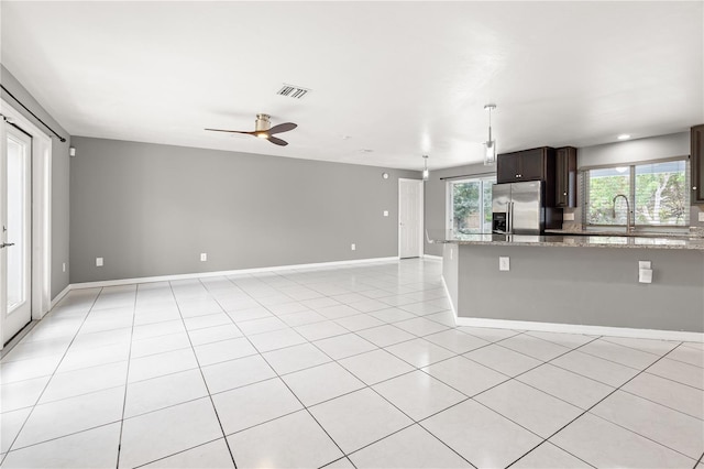 kitchen with light stone counters, light tile patterned floors, visible vents, dark brown cabinetry, and stainless steel fridge