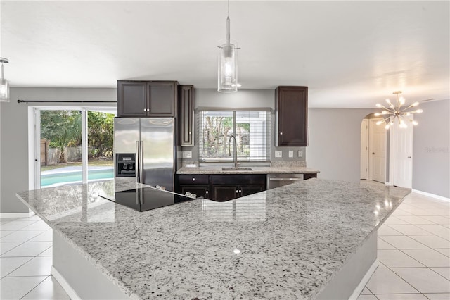 kitchen with stainless steel appliances, light stone counters, a kitchen island, and pendant lighting