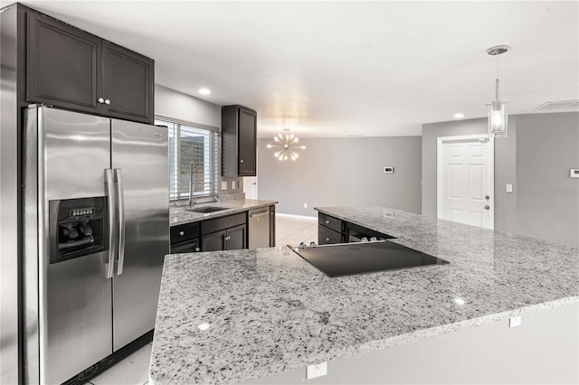 kitchen with appliances with stainless steel finishes, light stone counters, a sink, and decorative light fixtures