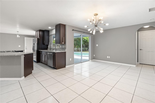 kitchen featuring light tile patterned floors, arched walkways, decorative light fixtures, light stone countertops, and stainless steel appliances