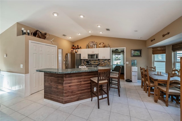 kitchen featuring vaulted ceiling, a center island with sink, light tile patterned floors, stainless steel appliances, and white cabinets