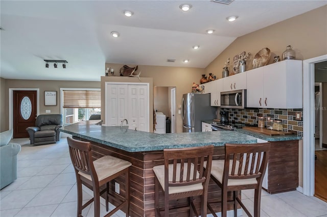 kitchen featuring a breakfast bar, vaulted ceiling, appliances with stainless steel finishes, washer / clothes dryer, and white cabinets