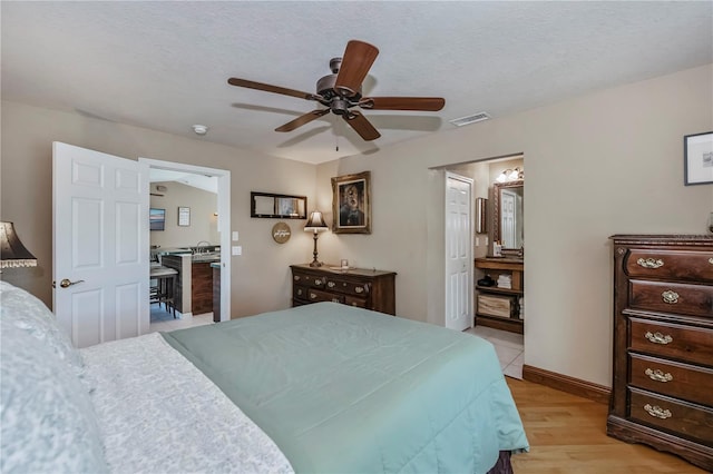 bedroom with ensuite bath, light hardwood / wood-style floors, ceiling fan, and a textured ceiling