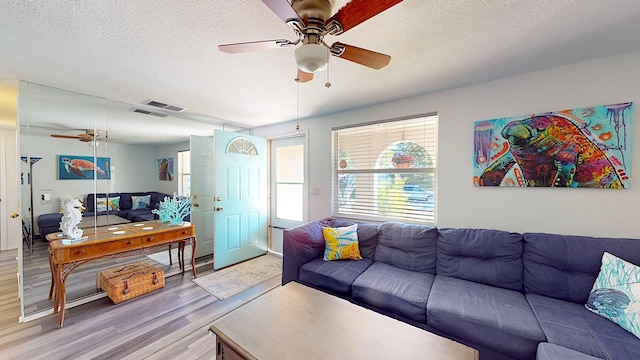 living room with a textured ceiling, ceiling fan, and light wood-type flooring