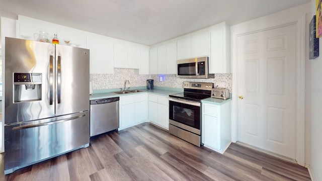 kitchen featuring appliances with stainless steel finishes, hardwood / wood-style floors, sink, white cabinets, and backsplash