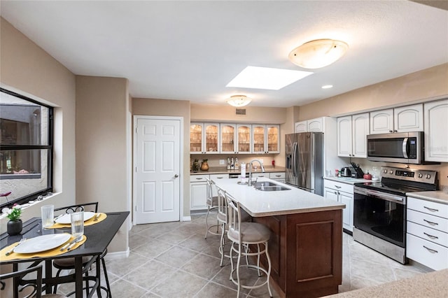 kitchen featuring appliances with stainless steel finishes, a skylight, sink, white cabinets, and a center island with sink