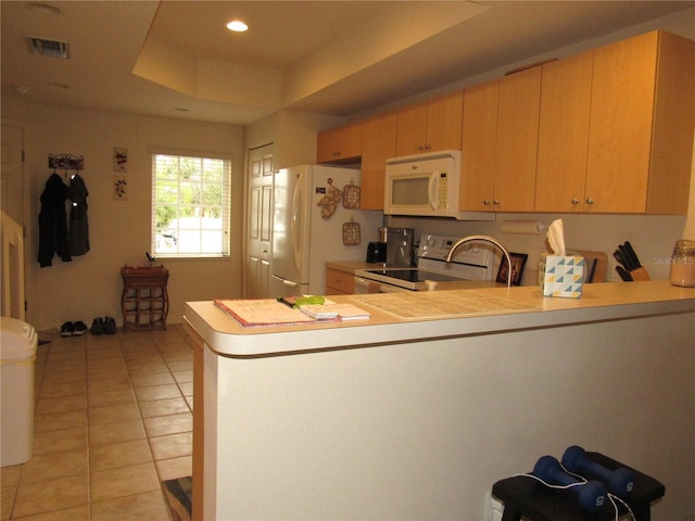 kitchen with a tray ceiling, white appliances, kitchen peninsula, and light tile patterned flooring