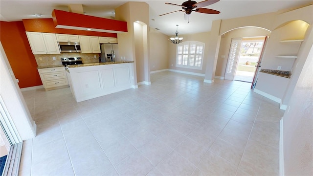 kitchen featuring ceiling fan with notable chandelier, white cabinetry, stainless steel appliances, decorative backsplash, and vaulted ceiling