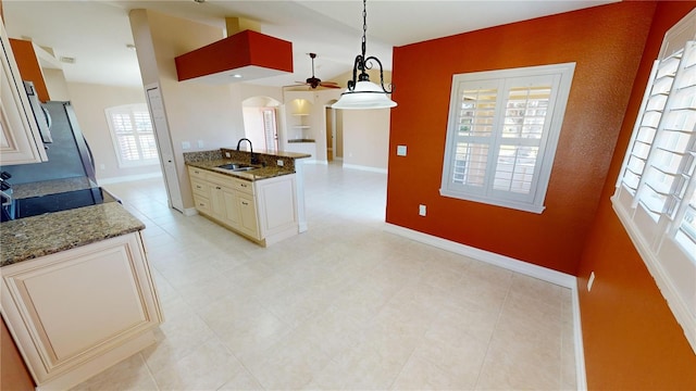 kitchen with sink, stove, stone countertops, decorative light fixtures, and cream cabinetry