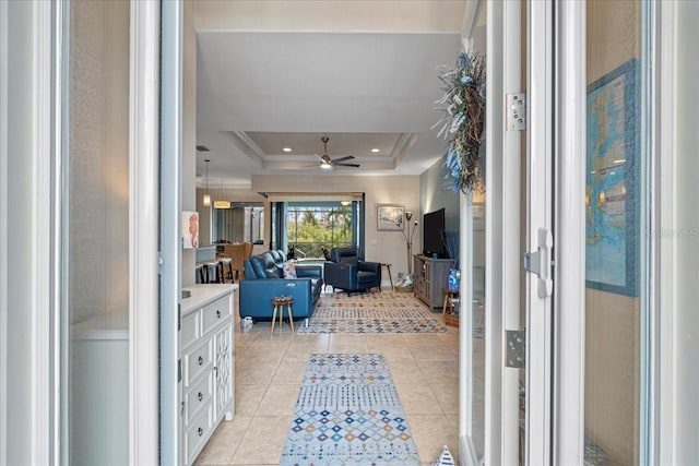 interior space with light tile patterned flooring, ceiling fan, ornamental molding, and a raised ceiling