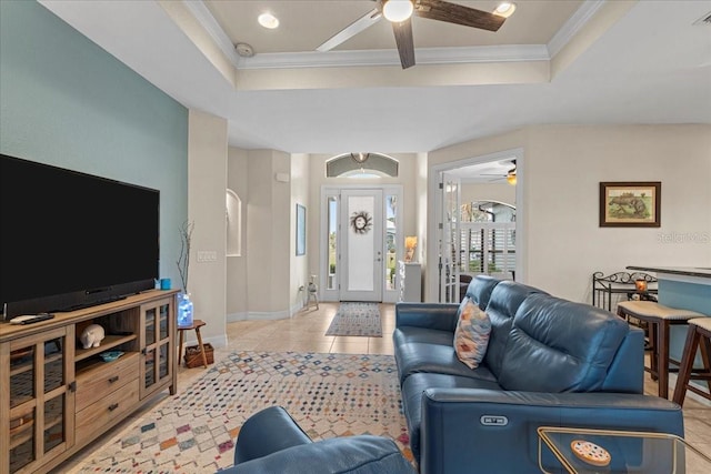 living room with crown molding, ceiling fan, a tray ceiling, and light tile patterned floors