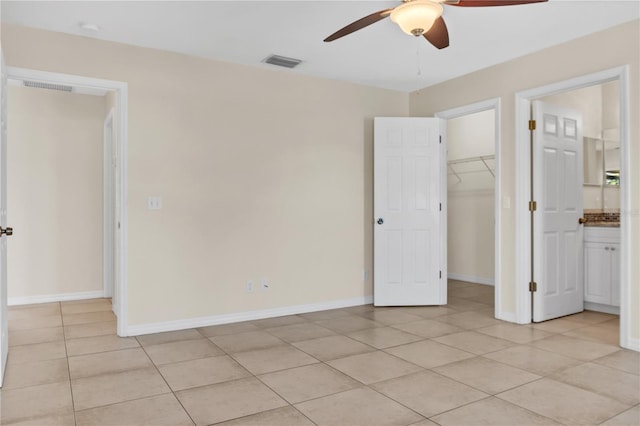 unfurnished bedroom with ensuite bath, ceiling fan, light tile patterned flooring, a walk in closet, and a closet